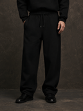 Model wearing black wide-leg sweatpants with a drawstring waist and black sweatshirt in a dark textured studio