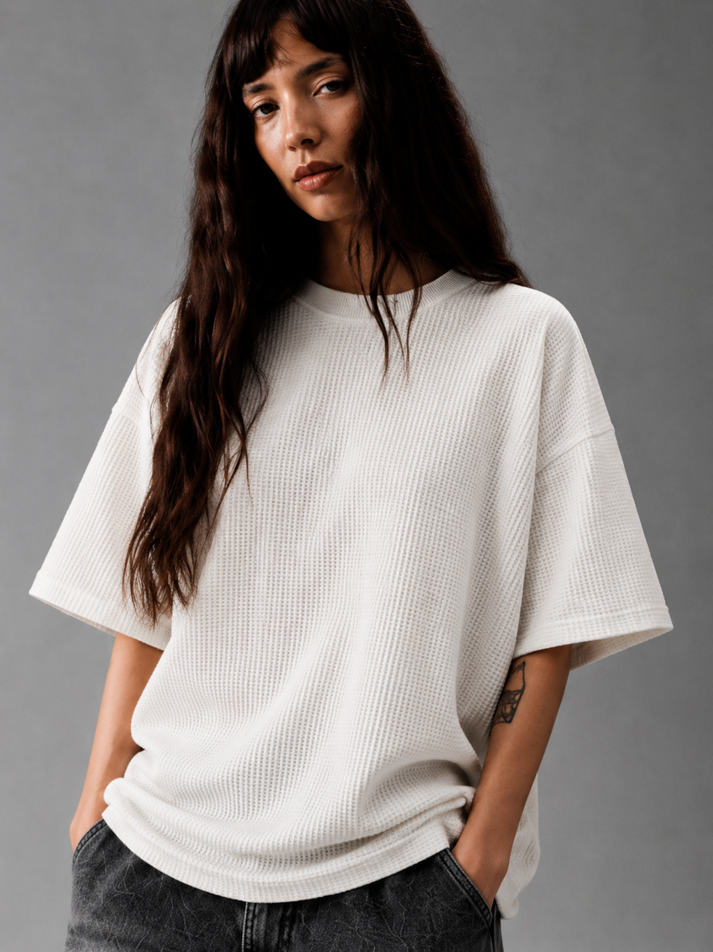 Woman wearing an off-white waffle knit oversized T-shirt with dark gray jeans in a minimalist studio