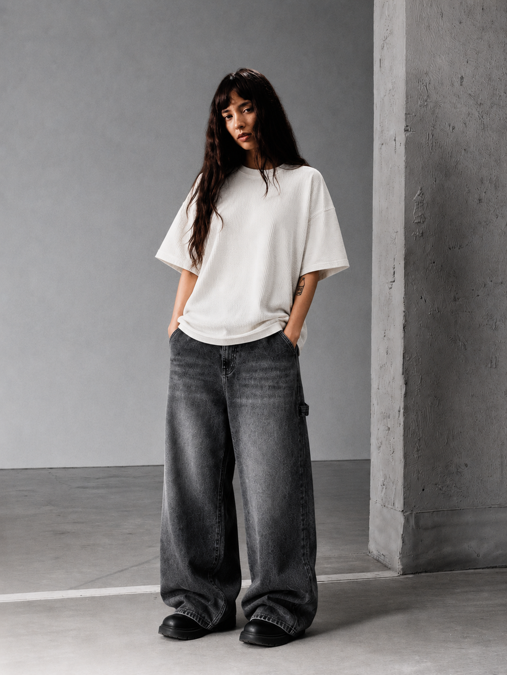Woman wearing an off-white waffle knit oversized T-shirt with wide-leg dark gray jeans in a minimalist concrete studio